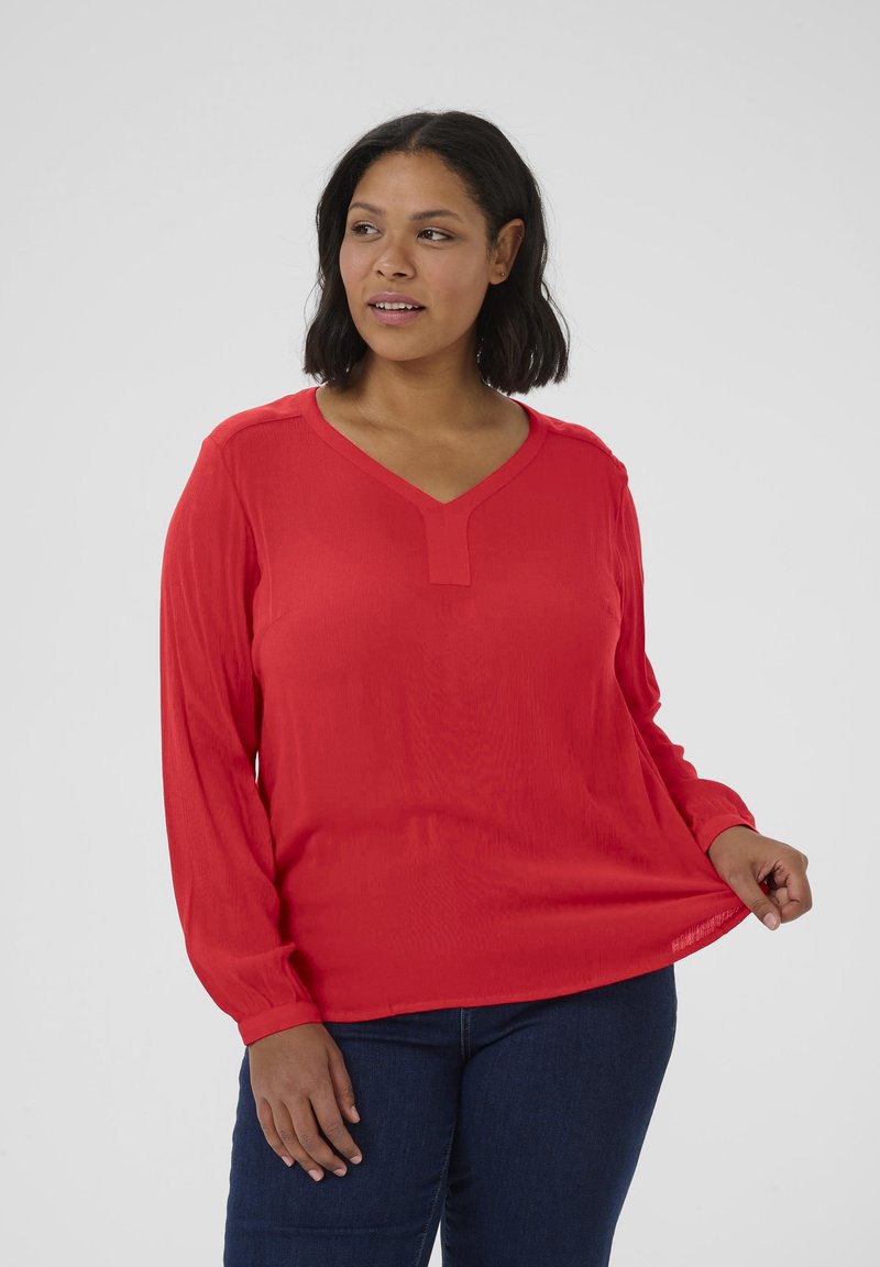 Blusa rossa a maniche lunghe con scollatura a V, caratterizzata da una sottile texture e una vestibilità rilassata, abbinata a jeans blu scuro.