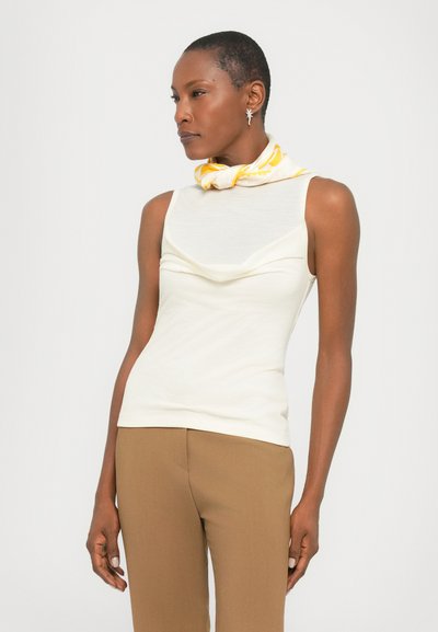 Sleeveless cream top with a draped neckline, paired with tan fitted pants and a yellow patterned scarf around the neck. Smooth texture.