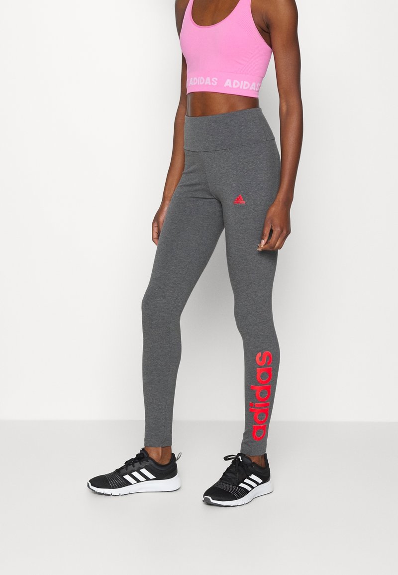 Grå leggings med en röd "adidas"-logotyp på vänster ben, tillsammans med en rosa sport-bh. Texturerat tyg, åtsittande design och hög midja.