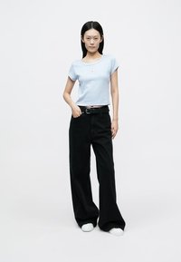 Light blue cropped t-shirt with ribbed neckline, paired with high-waisted black wide-leg pants. Model wearing white sneakers.