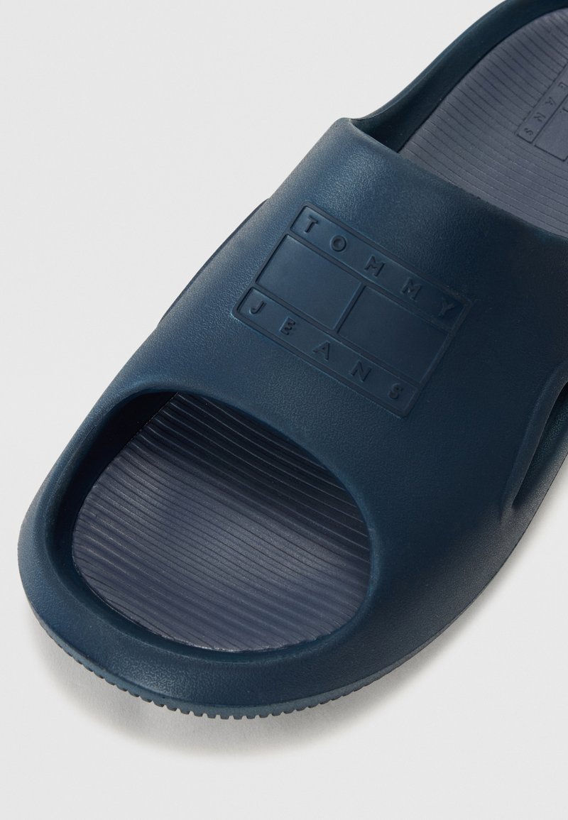Infradito blu navy realizzate in gomma testurizzata, con una fascia larga, punta aperta e logo "TOMMY JEANS" in rilievo sulla superficie superiore.