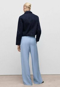 Dunkelblaue Jeansjacke im verkürzten Design mit Kragen, kombiniert mit hellblauen, weit geschnittenen Hosen aus glattem Material und mit Gesäßtaschen.