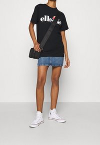 Camiseta de algodón negra con logo blanco, falda mini de mezclilla azul y zapatillas deportivas altas blancas. Pequeno bolso cruzado negro con correa ajustable.