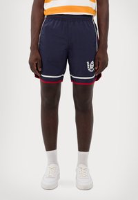 Marineblå shorts med hvid og rød kant, der har elastisk talje og et hvidt logo. Materialet ser let og glat ud.