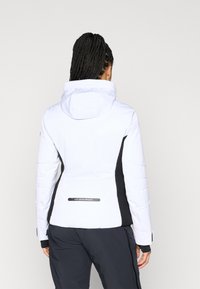 Λευκή σακέτα σκι με μαύρες πλευρές, κουκούλα και υφασμάτινα μανίκια. Διαθέτει λογότυπο στο πίσω μέρος και φερμουάρ στους καρπούς.