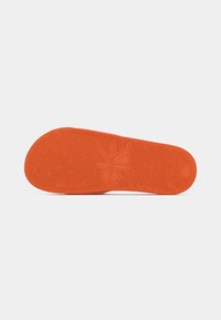 Orange gummisål med en tekstureret overflade og et logoaftryk. Designet har riller for greb og traction.