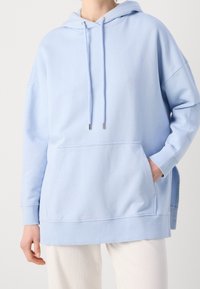 Hellblauer Hoodie aus weichem Stoff, mit einer Fronttasche, Kapuze mit Kordelzug und gerippten Bündchen. Lässige Passform mit seitlichen Schlitzen.