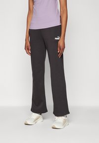 Donkergrijze, losse sweatpants met een witte PUMA-logo. Gecombineerd met een lichtpaarse tanktop en sportieve schoenen.