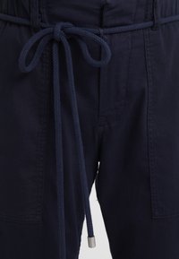 Marina blå tygbyxor med en strukturerad yta, utrustade med ett knytband i midjan och en strömlinjeformad design. Inkluderar sidfickor för funktionalitet.