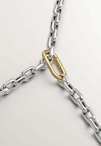 Cadena de metal con eslabones plateados entrelazados, un eslabón dorado alargado conectando dos secciones, superficie lisa y acabado brillante.