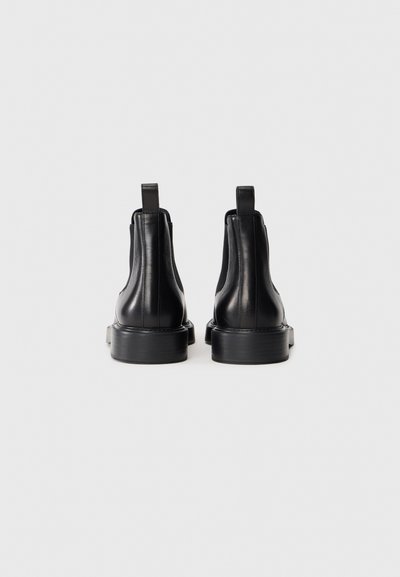 Svarta läderankelboots med en slät yta, elastiska sidopaneler och platta gummisulor. Bakre dragflikar för enkel påtagning.