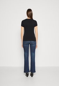 Camiseta negra ajustada combinada con vaqueros de campana azul oscuro y tacones negros. Tejido suave, diseño sencillo, con un escote clásico y mangas cortas.