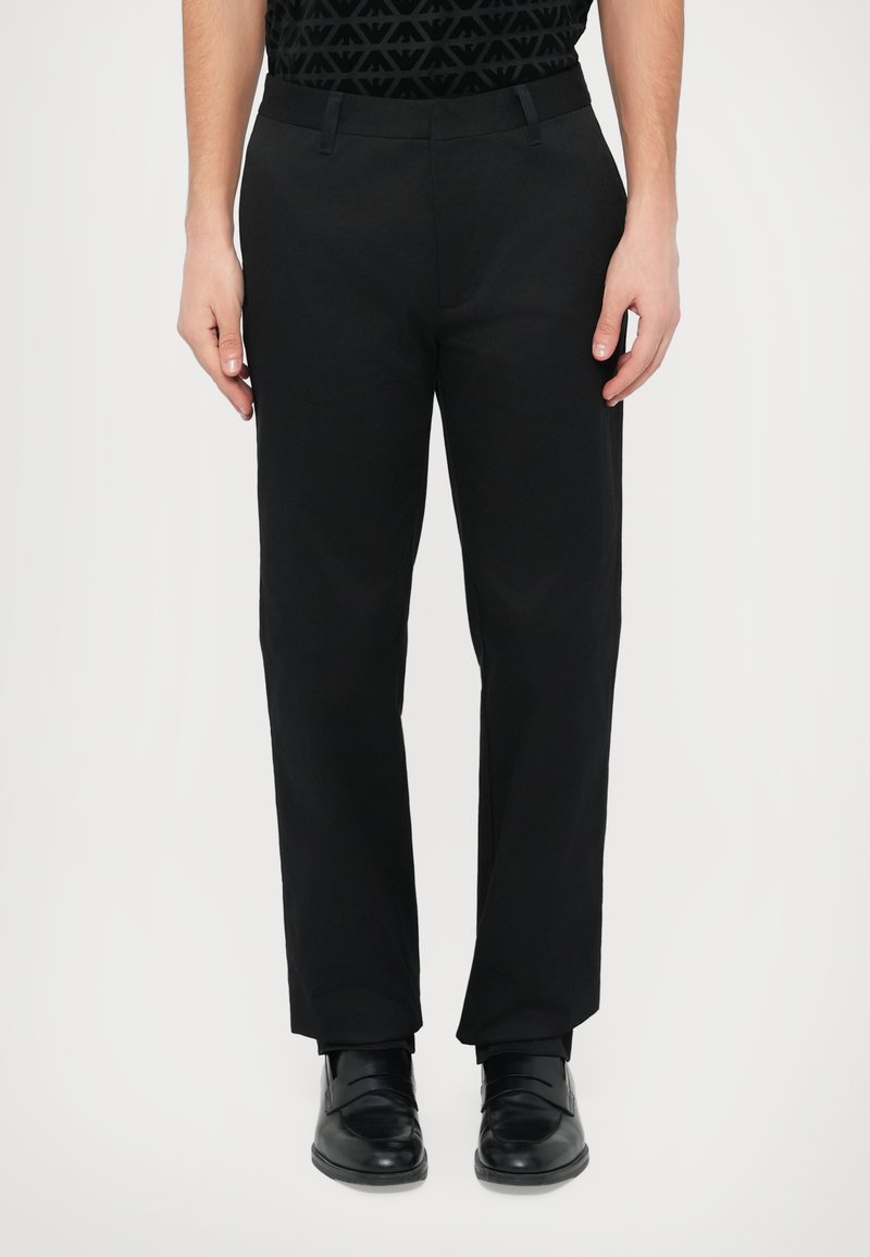 Čierne nohavice so sviežim strihom, vyrobené z hladkej látky, s bočnými vreckami a zapínaním na zips. Nosené s čiernymi topánkami.