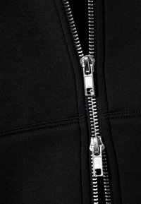 Μαύρο μπουφάν με φερμουάρ διπλού μεταλλικού τύπου, λείο ύφασμα και ενισχυμένες ραφές. Κοντινό του φερμουάρ και της υφής του υφάσματος.