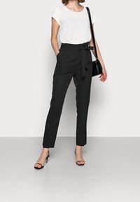 Zwarte, hoge broek met een belted taille, zijzakken en een op maat gemaakte pasvorm, gecombineerd met een witte top met korte mouwen en zwarte sandalen.