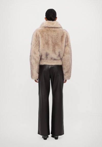 Chaqueta de piel sintética con un amplio cuello, color beige y corte relajado. Combinada con pantalones de cuero negro de talle alto, de textura suave.