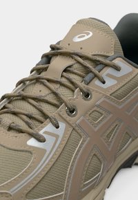 Αθλητικό παπούτσι σε μπεζ και ταμπά χρώμα με υφαντό ύφασμα, πλαστικές επικαλύψεις, κορδόνια με σχέδια και λευκό λογότυπο στη γλώσσα.