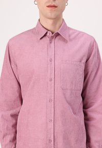 Pink corduroy button-up shirt with a pointed collar, long sleeves, and a single patch pocket on the left side. Vertical ribbed texture.