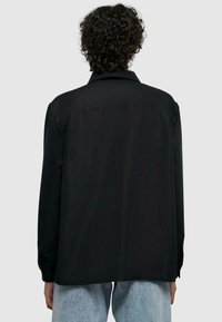 Zwarte langemouwen shirt met kraag, met een rechte snit en knoopmanchetten. Het materiaal lijkt glad met een matte afwerking.