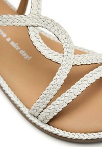 Sandal in bianco con intrecci, dal design piatto, con soletta color tan e suola cucita. Il testo sulla soletta recita "Buona giornata!"
