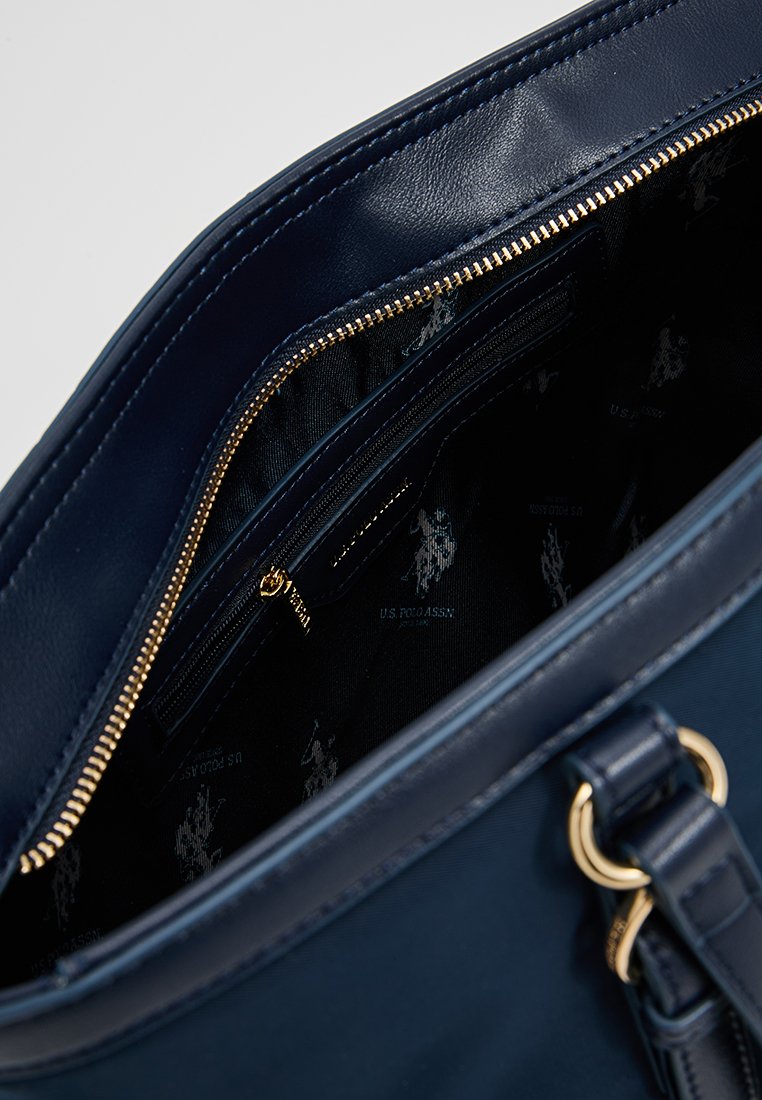 Intérieur d'un sac à main en cuir bleu marine avec une fermeture éclair dorée, présentant plusieurs compartiments et un revêtement en tissu sombre avec un motif de logo.