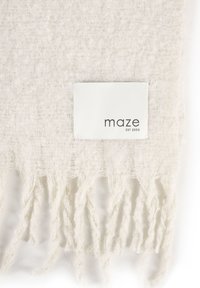 Biały, teksturowany, tkany materiał z postrzępionymi krawędziami i prostokątną etykietą z napisem "maze EST 2003" przyszytą blisko dolnego środka.