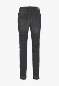 Svarta denimjeans med smal passform; bakvyn visar två påsydda fickor och subtila blekningar längs benen. Rent avslut på fållen.