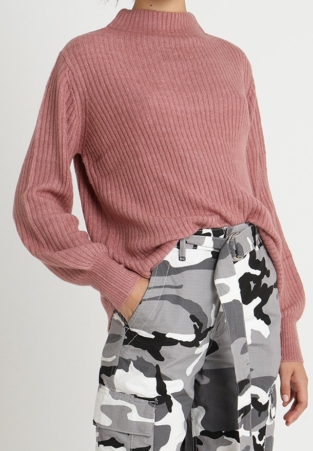 Pull à manches longues en maille côtelée rose poudré associé à un pantalon cargo camouflage blanc, gris et noir taille haute avec une ceinture en tissu.