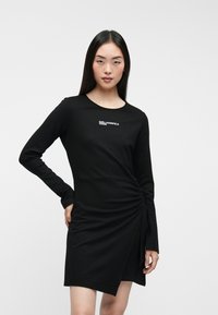 Must mustriga kleit, millel on keha kummardav siluett, keeratud disainiga detail vööl ja rinnal peene valge logo print.