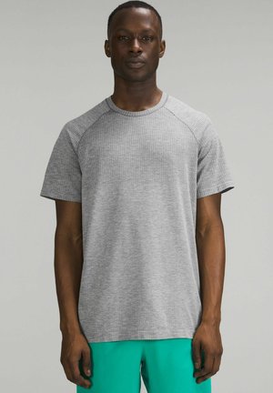 Šedé tričko s krátkým rukávem a texturovaným povrchem, s raglánovými rukávy, vystavené na neutrálním pozadí, doplněné tyrkysovými šortkami.