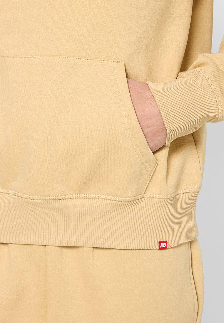 Sudadera amarilla clara con un bolsillo tipo canguro, puños y dobladillo acanalados, y una pequeña etiqueta de logo roja en el lado izquierdo.