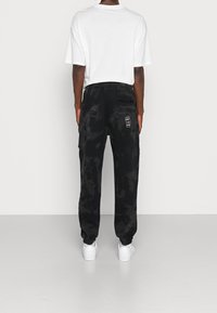 Black tie-dye joggers with elastic waistband and cuffed ankles. Features a patch pocket and embroidered fist logo on the rear.