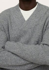 Grauer, gestrickter Pullover mit V-Ausschnitt, der über einem weißen Unterhemd getragen wird. Er hat eine gerippte Struktur und lange Ärmel.