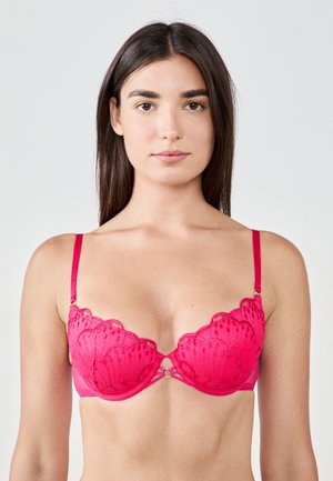 Reggiseno di pizzo rosa con bordi ondulati, coppe trasparenti e hardware decorativo centrale. Le spalline sono regolabili e il materiale appare liscio e morbido.