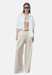 Vit linne skjorta, beige ribbad crop top och vida krämfärgade byxor med ett glänsande silverbälte. Modellen bär svarta solglasögon.