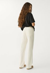 Krämfärgade byxor med vida ben i denim, med hög midja, två bakfickor och trasiga fållar. Bärs med en svart T-shirt.