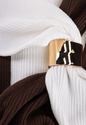 Wit en bruin geribbeld stof samen gedraaid en vastgezet met een glanzende gouden metalen ring.