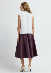 Weiße, ärmellose Bluse mit Kragen, kombiniert mit einem knielangen, ausgestellten lila Kunstlederrock. Das Model trägt beige High Heels.