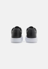 Schwarze Leder-Sneaker mit weißen Gummisohlen, die ein minimalistisches Design und ein geprägtes Logo an der Ferse aufweisen. Glatte Textur.