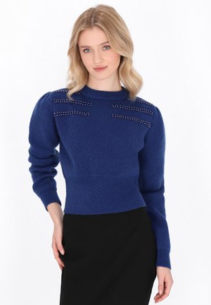 Maglione blu lavorato a maglia con scollatura rotonda e maniche a sbuffo. Presenta dettagli con borchie in linee orizzontali sulle spalle.