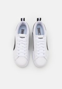 Valged sneake' ridaga mustade aktsentidega, millel on sile sünteetiline ülemine osa, ümar varvas, lame paelad ja madal disain. Logo keele peal.