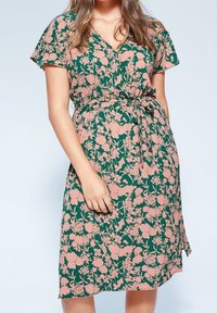 Vestido de corte envolvente en tejido verde con flores rosas. Cuenta con mangas cortas, un escote en V y un cinturón en la cintura para un ajuste ceñido.