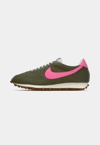 Olivu zaļas sporta kurpes ar rozā Nike zīmolu, teksturēts augšdaļa, baltas auklas un brūns gumijas zole. Sānu viedoklis, slaids dizains.
