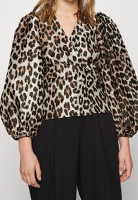 Blouse en satin imprimé léopard avec manches ballon, dotée d'une coupe portefeuille. La palette de couleurs comprend l'or, le noir et le crème.