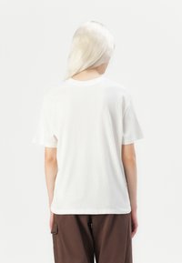 Hvit t-skjorte med korte ermer og rund hals, laget av mykt stoff. Baksiden er ensfarget uten synlige logoer eller mønstre.