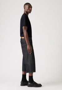 Camiseta de algodón negra combinada con una falda de mezclilla oscura hasta la mitad de la pantorrilla. Presenta costuras visibles, bolsillos y mocasines negros con calcetines acanalados.