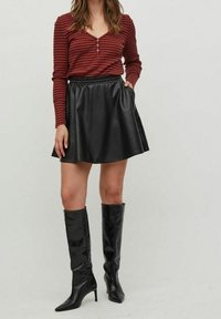 Top de manga larga con rayas rojas y botones, combinado con una falda acampanada de cuero sintético negro. Botas negras de tacón hasta la rodilla completan el conjunto.