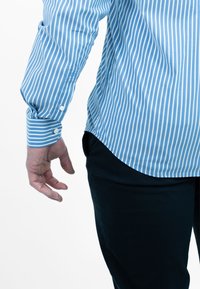 Lichtblauw en wit gestreept shirt met lange mouwen, voorzien van knoopmanchetten en een afgeronde zoom, gecombineerd met een donkere broek.