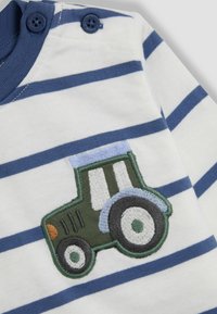 Gestreifte Baumwollbluse in Blau- und Weißtönen, mit einem grünen, gestickten Traktor-Design auf der Brust und Knopfdetails am Kragen.