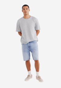 Šedé a bílé pruhované tričko, modré denimové šortky, béžové tenisky a bílé ponožky. Pohodlný outfit s volným střihem a minimalistickým designem.